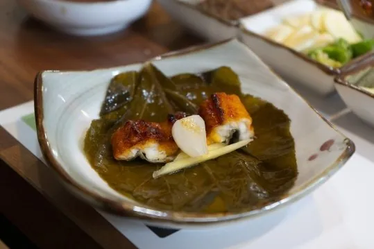 장아찌 잎 위에 올린 장어구이 두 점과 마늘