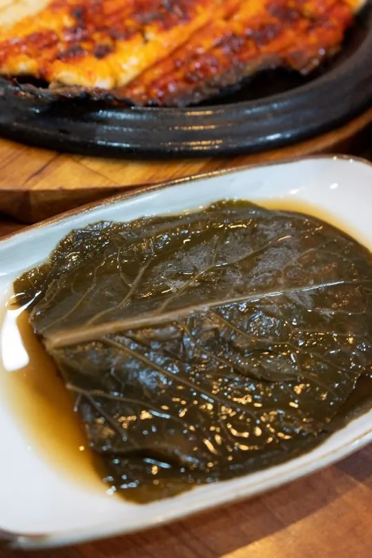접시에 담은 장아찌 잎, 뒤로 무쇠판 양념구이